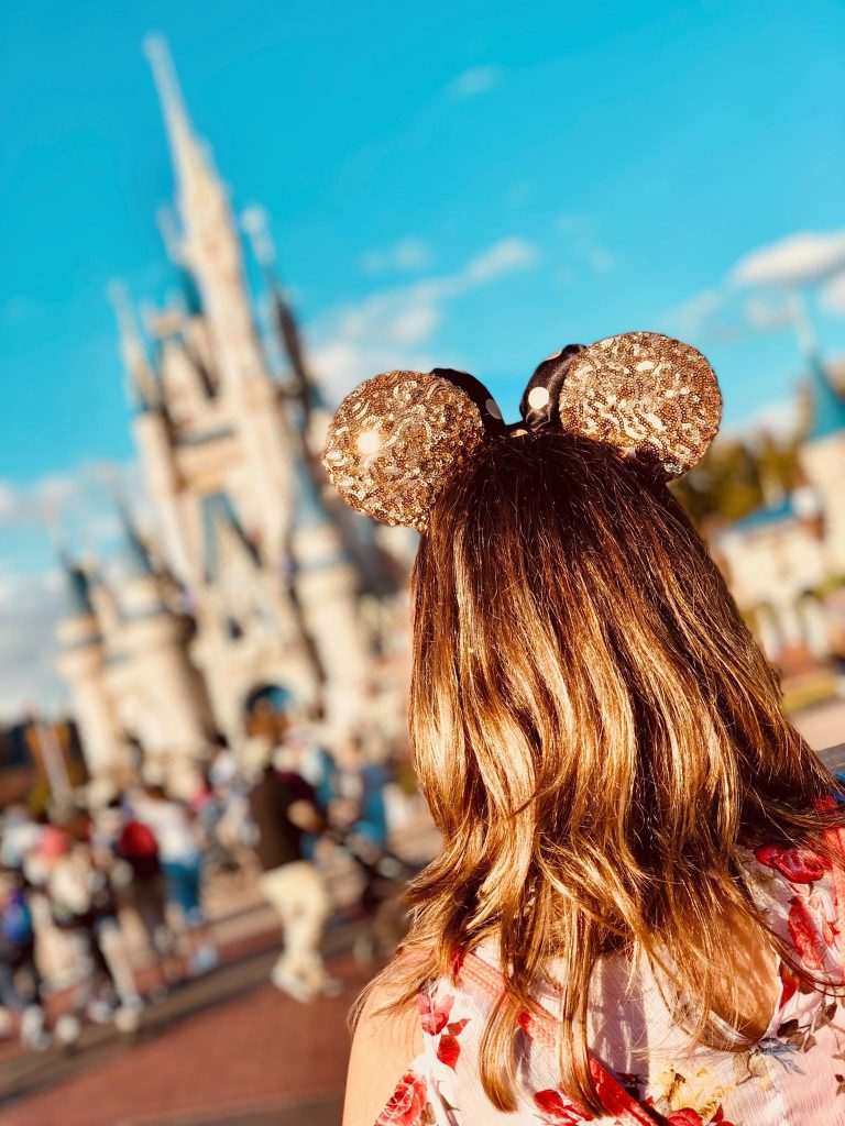 girl wearing mickey ears in front of castle 