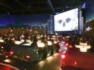theater with fake vintage cars and a screen playing an old black and white movie