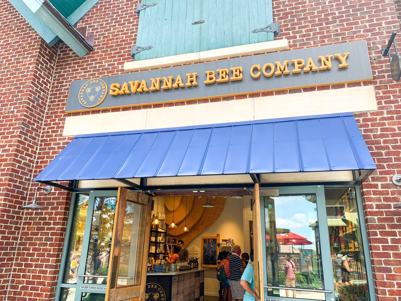 Storefront of the Savannah Bee Company - a brick building with a blue awning and yellow letters on a grey background