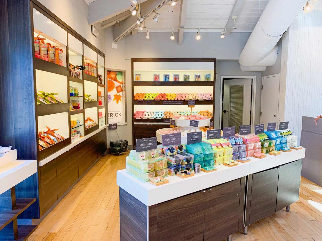 Multi colored soaps displayed on a table in the foreground, with other bath products displayed on shelves in the background