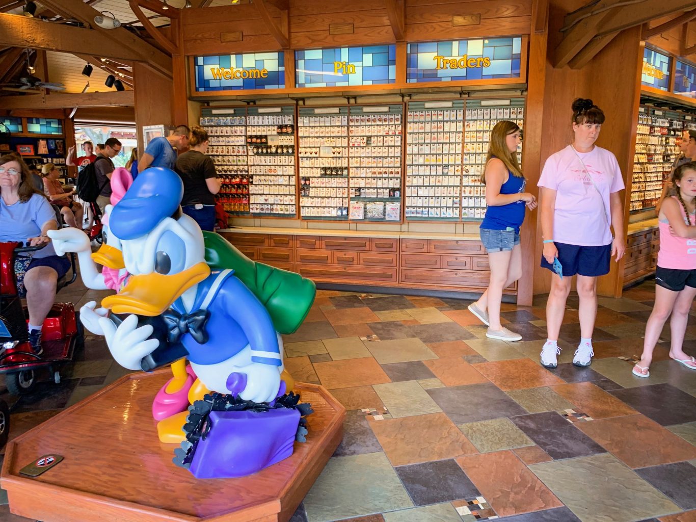 Inside of the Pin Traders store at Disney Springs with Donald Duck in the foreground and two people shopping in the background