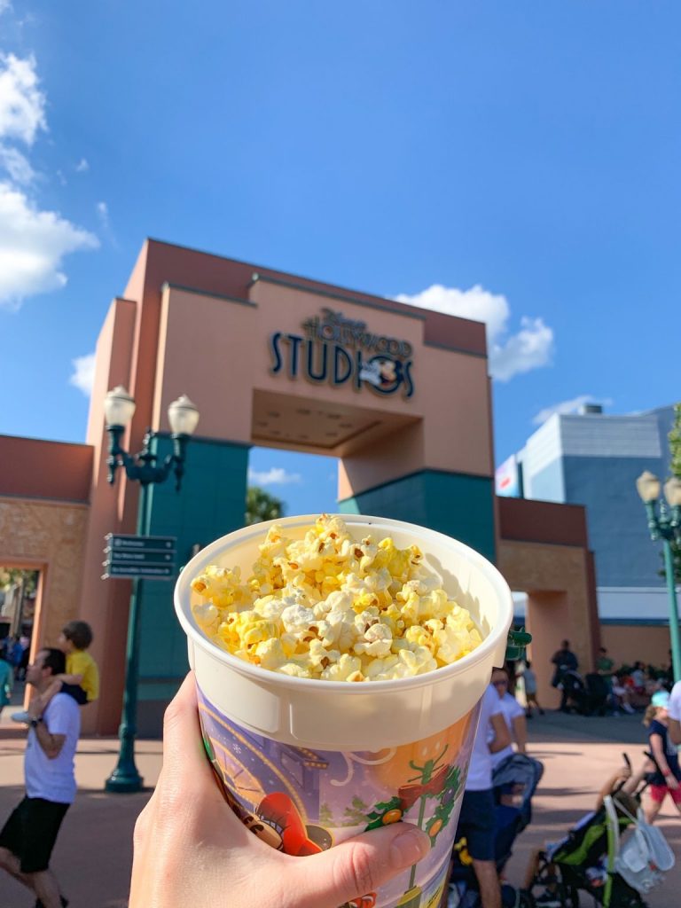 hand holding popcorn bucket in front of hollywood studios sign