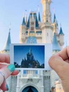 woman holding a polaroid picture of Cinderella's Castle in front of Cinderella's castle