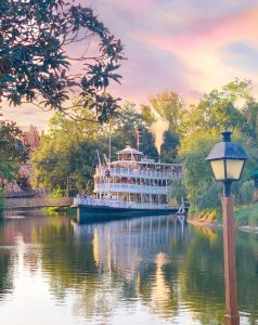 three tiered riverboat cruising on a river at sunset