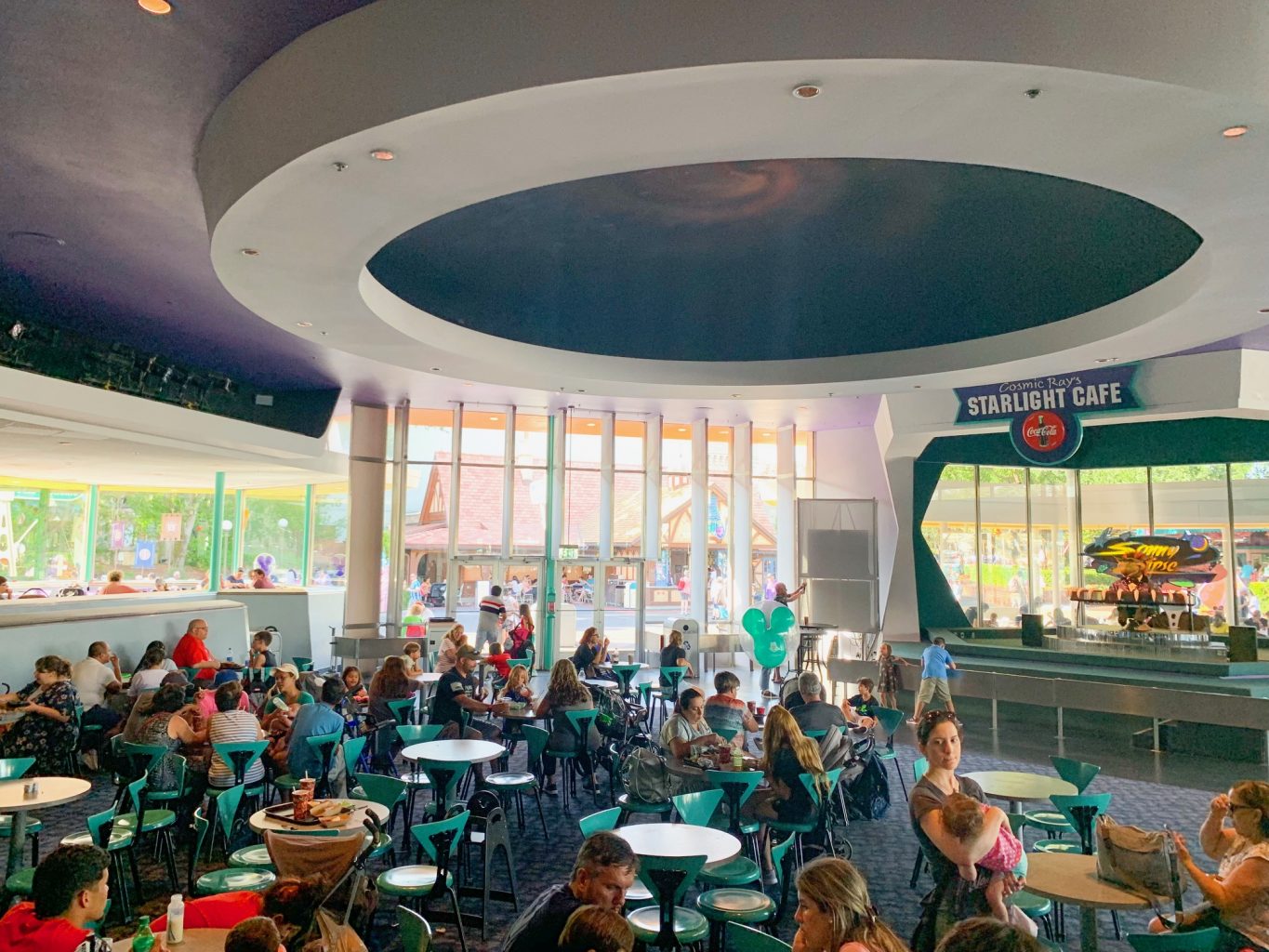 A room filled with people in green chairs and large spaceship-like circle on the ceiling is a common sight at Cosmic Rays, one of the best Magic Kingdom restaurants.