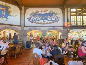 A busy dining area with a Pinocchio mural above crowded tables is a usual site at the Pinocchio Village. However, this is not one of the best Magic Kingdom restaurants-- eat elsewhere!