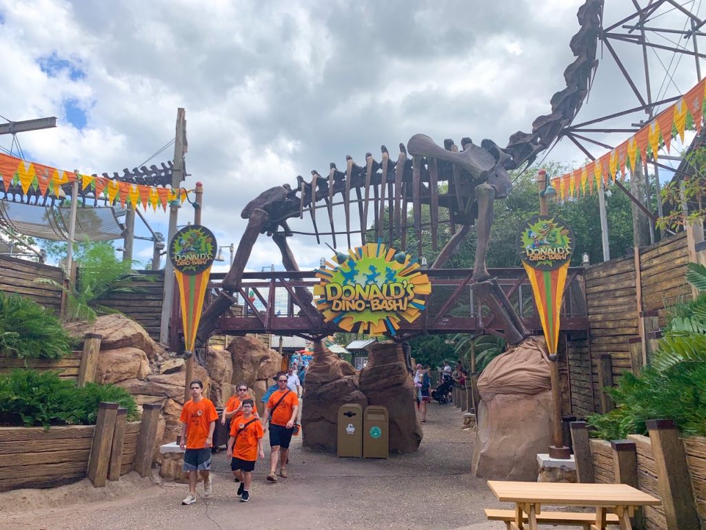 family walking in front of giant dino skeleton and signs for a party best Animal Kingdom rides