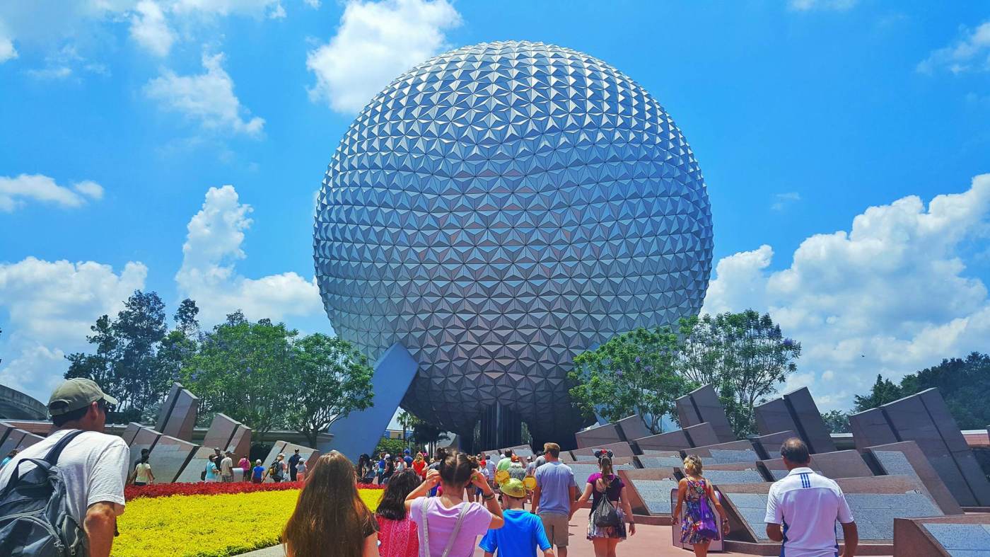 people in front of large silver ball spaceship earth