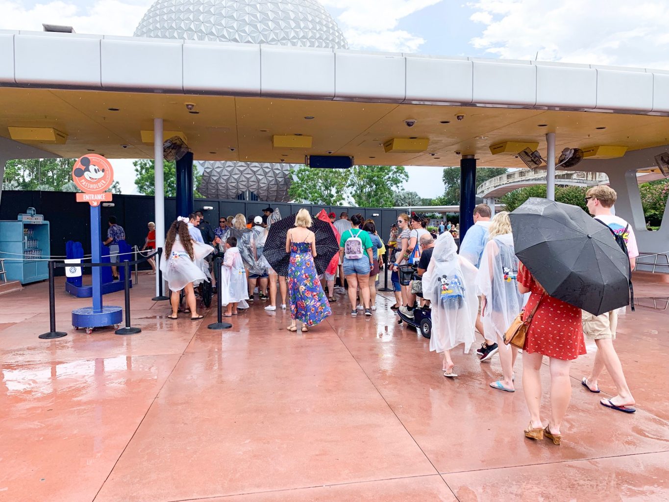 people in ponchos and under umbrellas in line disney on a budget