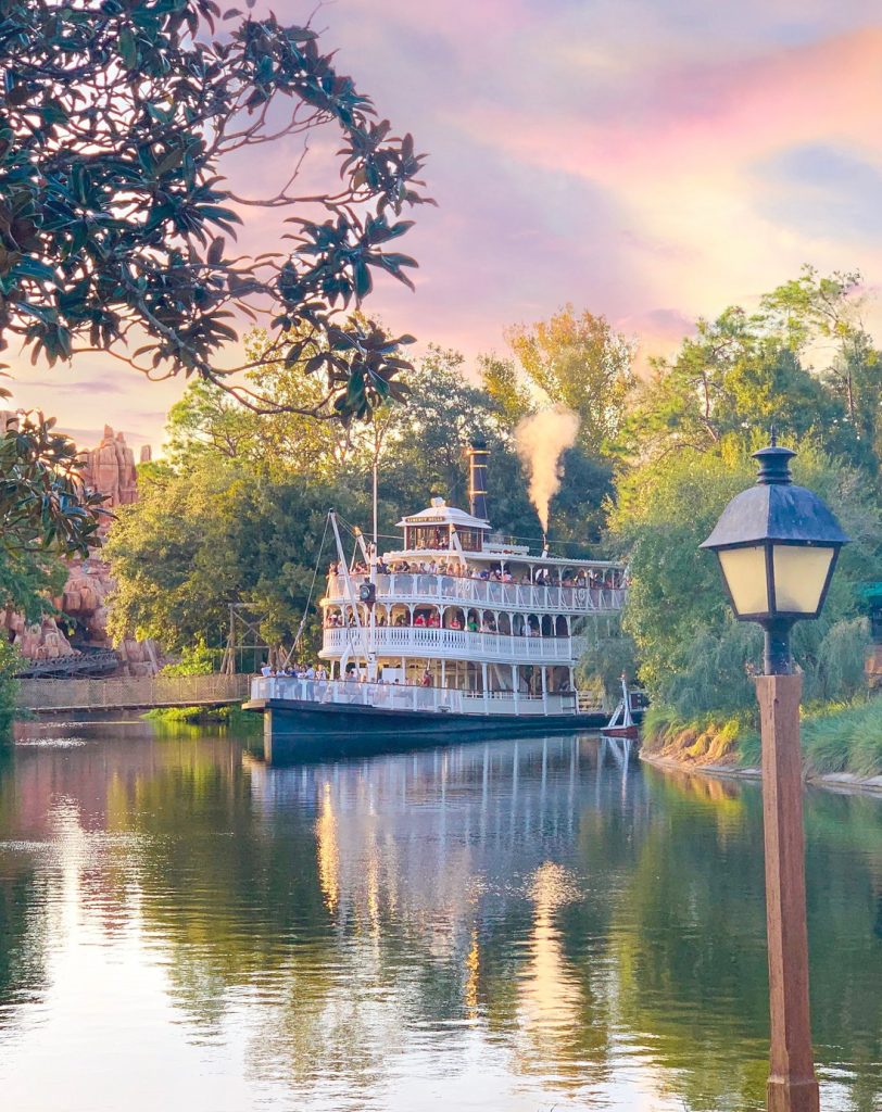 white riverboat coming around corner surrounded by trees on river 