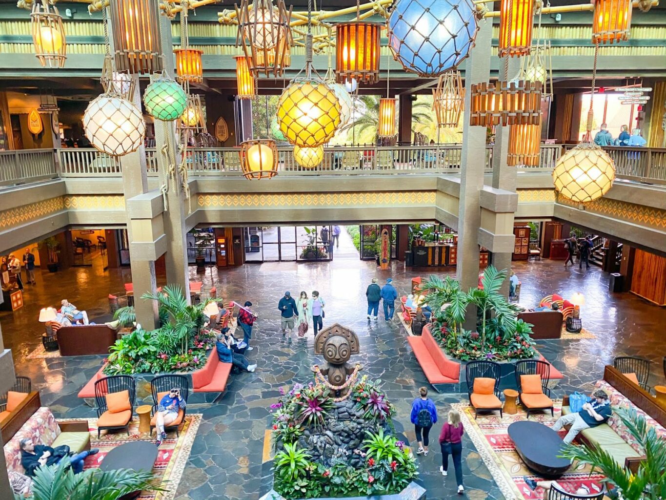 people walking around Polynesian themed lobby with statue and plants