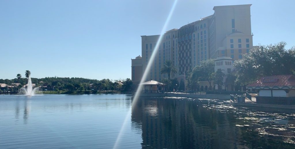 large yellow hotel tower on a lake with a fountain and sunlight best Disney World resorts