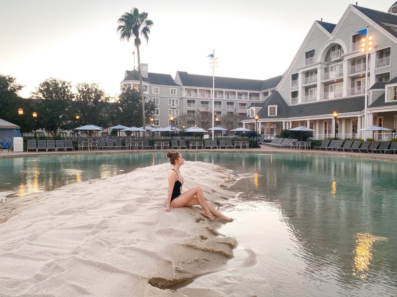 woman sitting on sand in front of water and large blue hotel building best Disney World resorts
