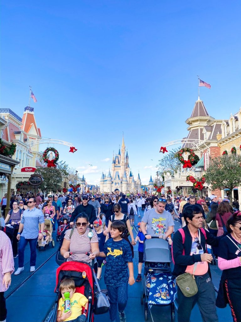 A photo of crowds of families with strollers walking down Main St USA with the castle in the background: there are lots of strollers, showing Disney with toddlers is possible even in crowds!