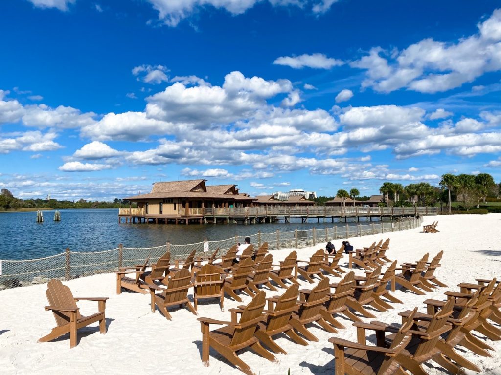 photo of wooden deckchairs on a white sandy beach, in front of wooden, over-water huts; rent DVC points at Disney Deluxe resort