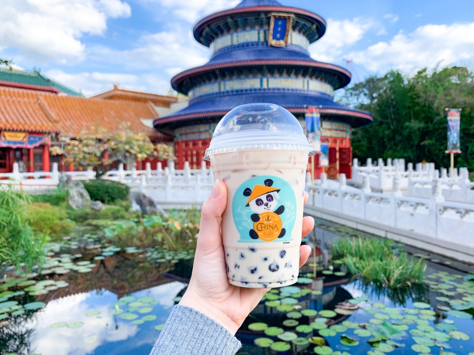 hand holding bubble tea drink in front of Chinese pavilion and water 