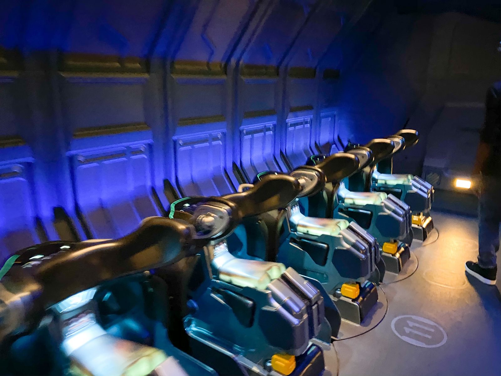 Green and black ride vehicles in front of blue wall for flight of passage ride