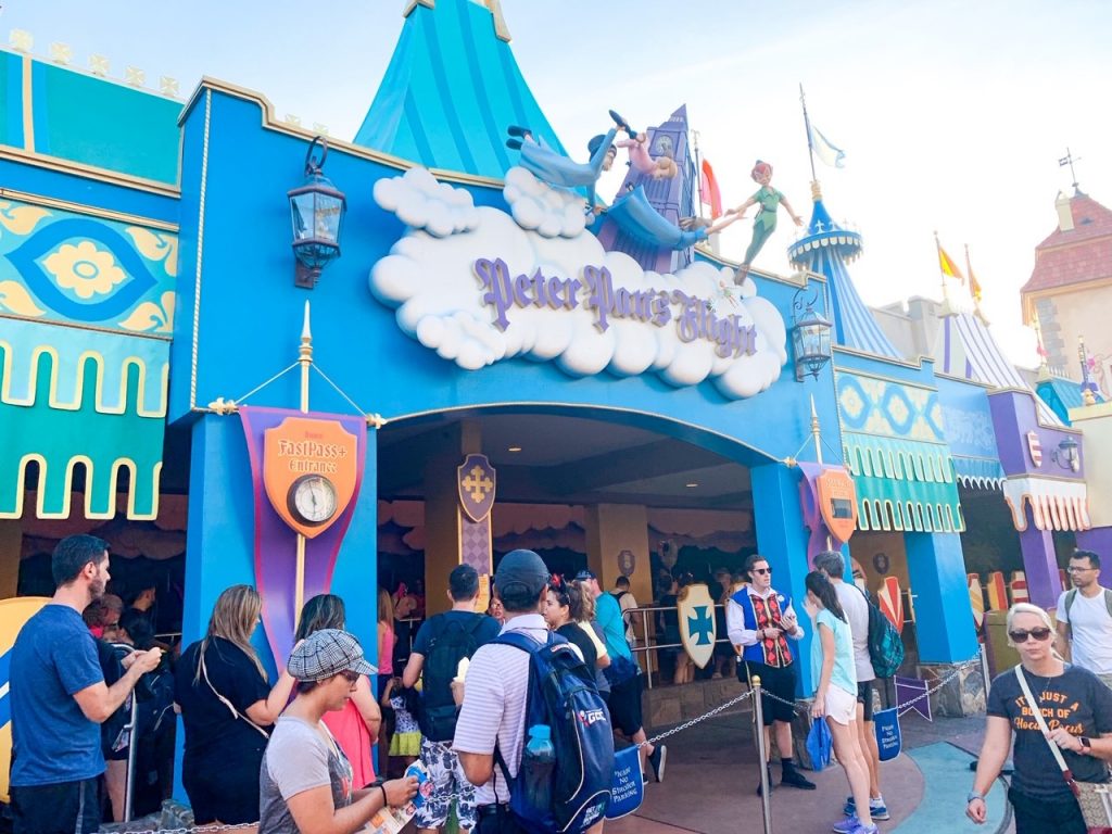 people in line for ride under big blue building and white sign 