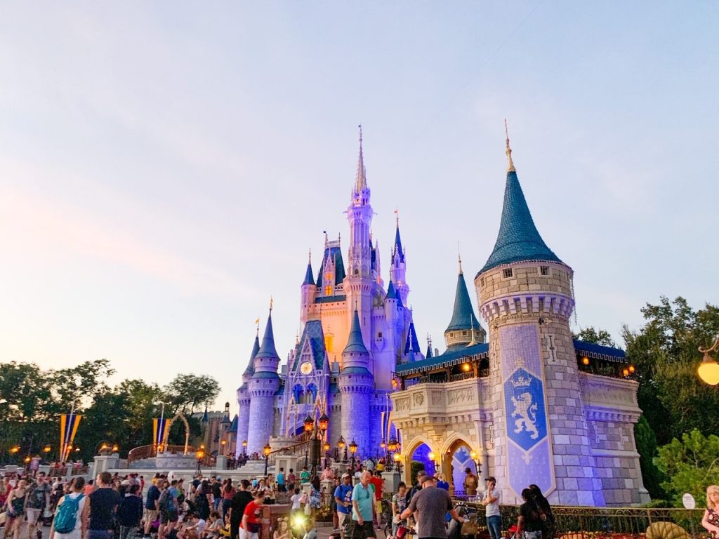 blue and pink storybook castle with a crowd in front of it and the sunsetting on it 
