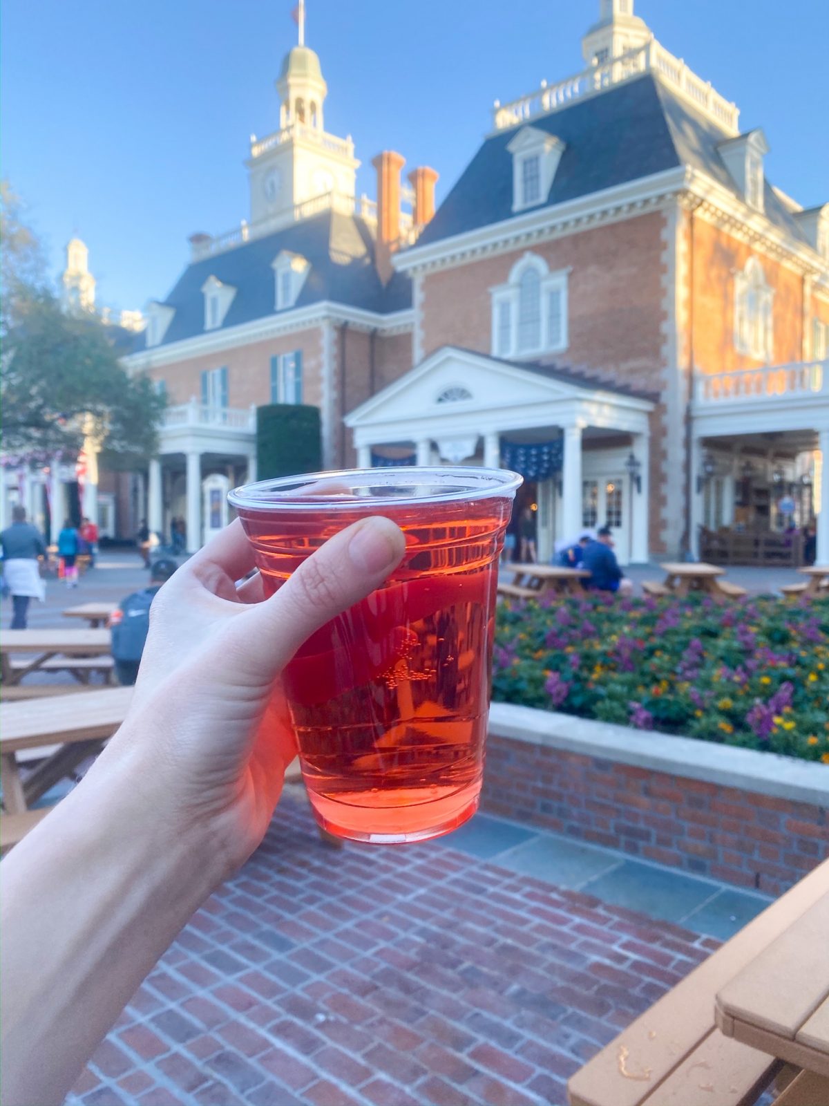 womans hand holding up Rose Hard Cider beer in Epcot with flowers in the background