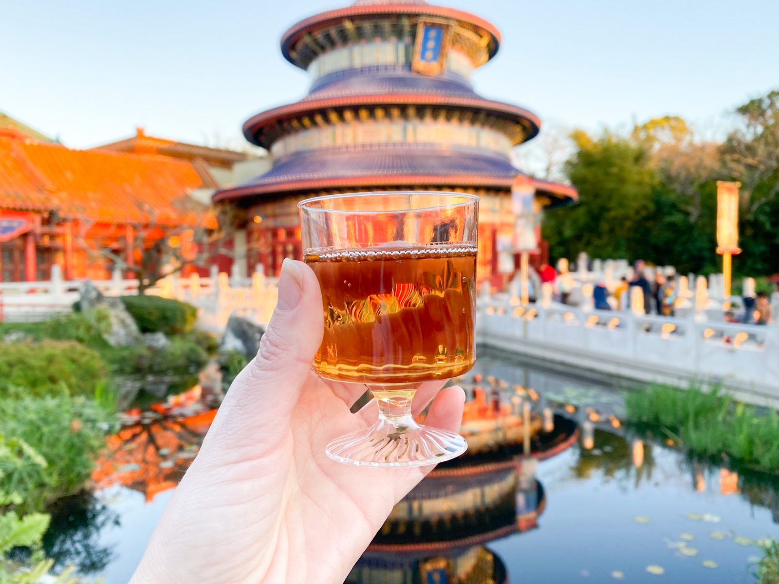 woman holding glass of Plum Wine In Epcot China with people in the background