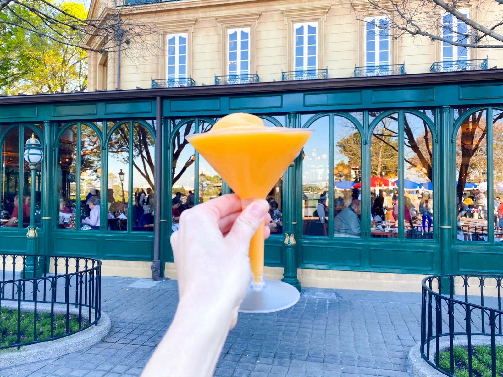 hand holding orange Grand Mariner Slush drink at Epcot drink around the world with people eating in the background