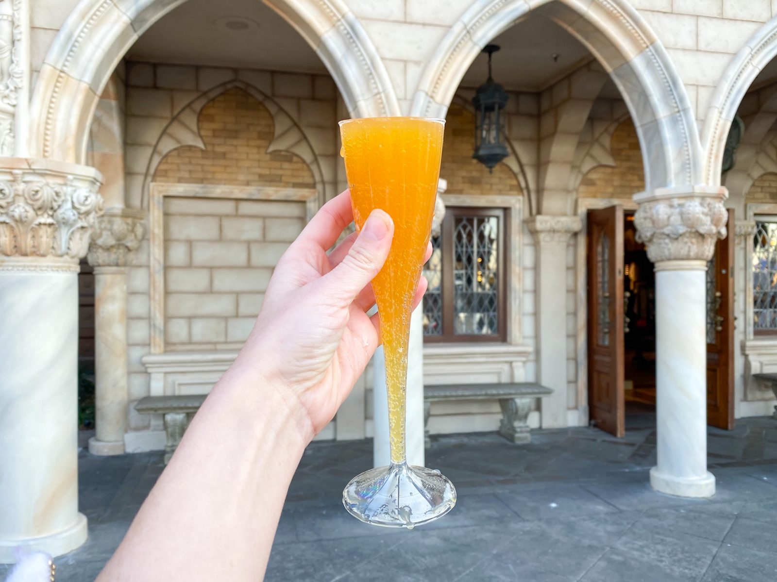 hand holding up a bellini against italian architecture while drinking around the world at disney's epcot