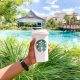 An outstretched hand holds the classic Starbucks designed cup with a beautiful Floridian backdrop complete with aqua blue water and palm fronds.