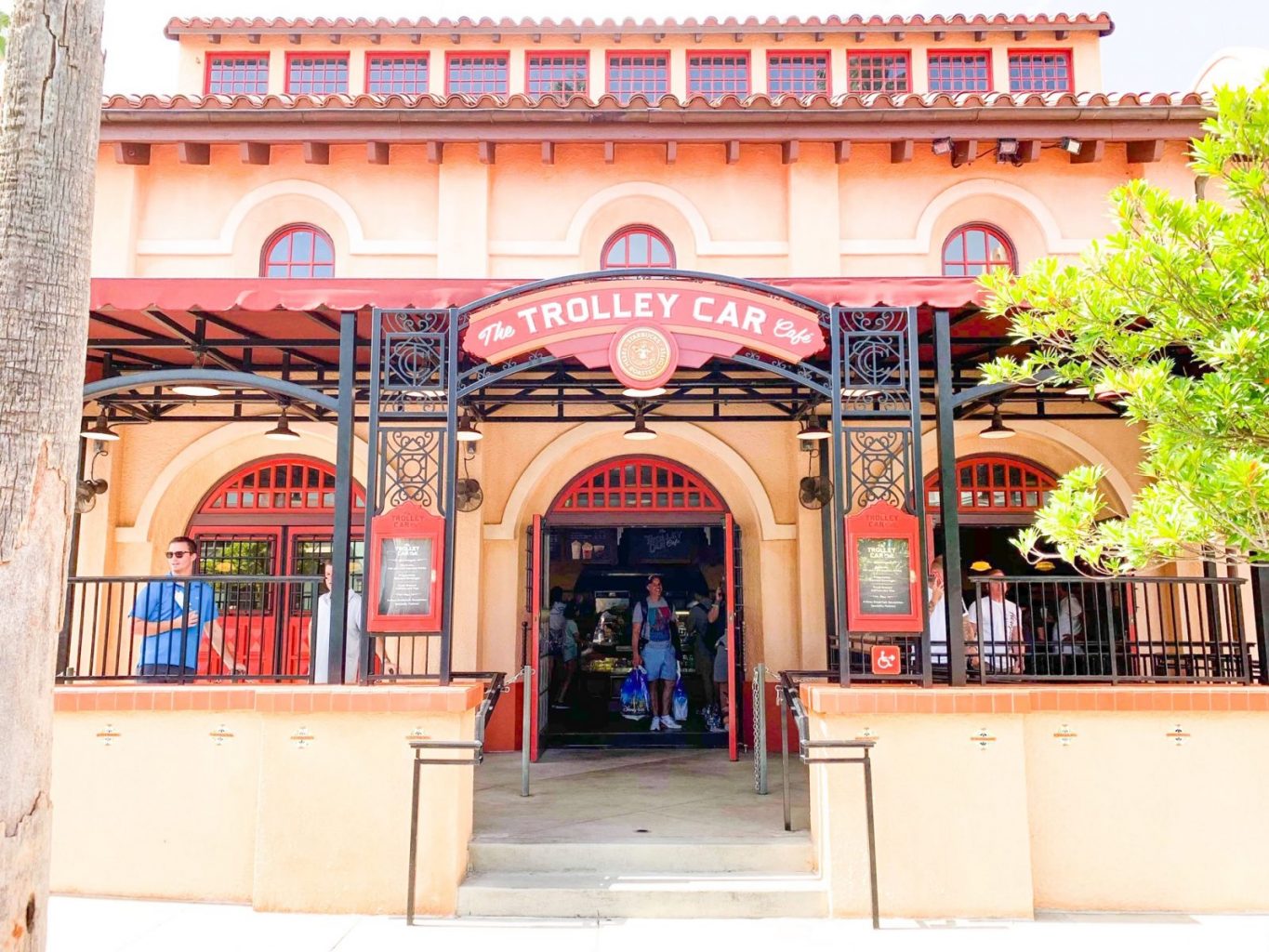 We see the front and entrance of the Trolley Cafe at Hollywood Studios, Walt Disney World. It is designed to look like a golden age trolley station. with tall walls and arched doors and windows.