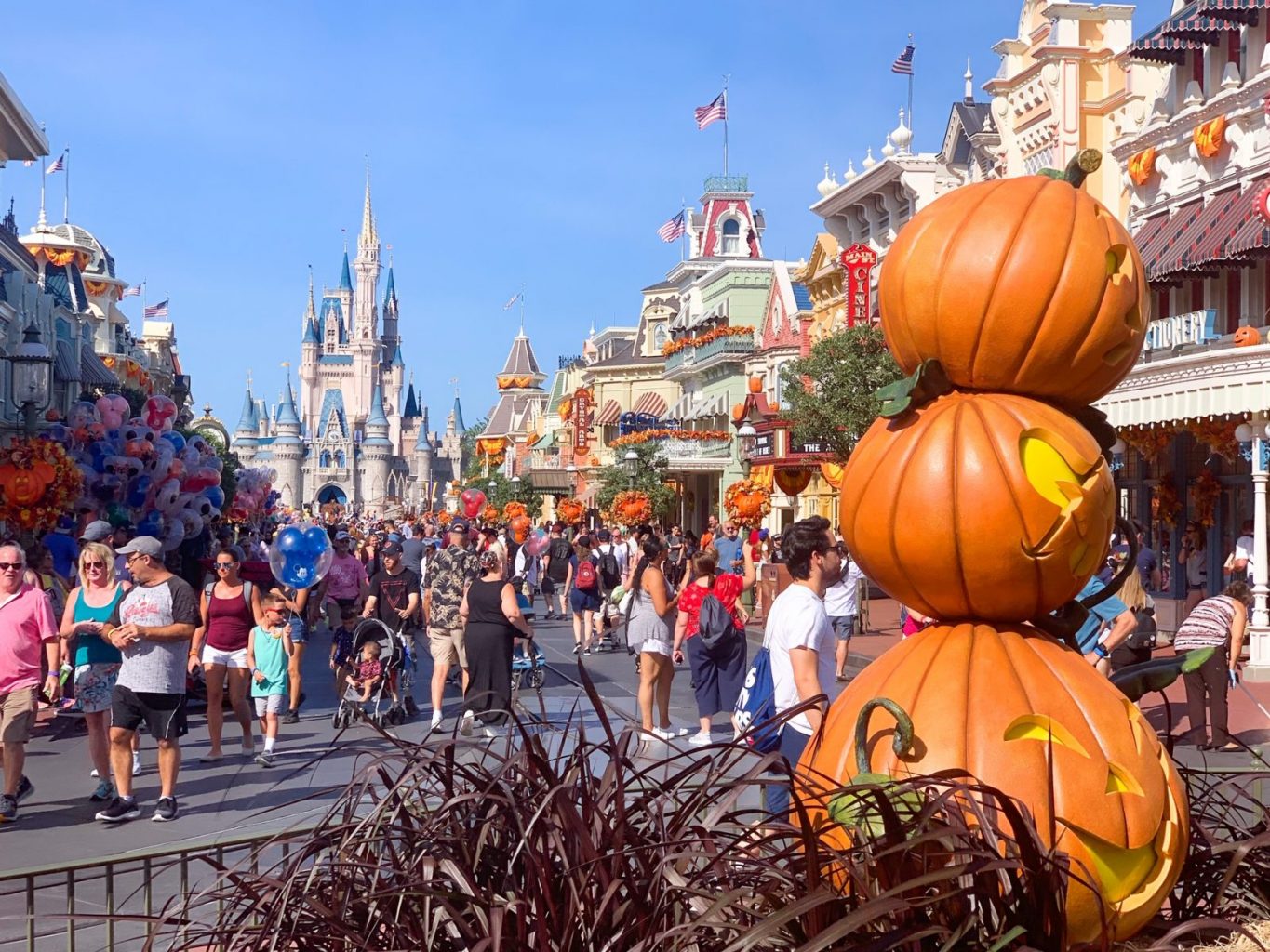 view of main street as people walk down the street next to pumpkin decorations in magic kingdom