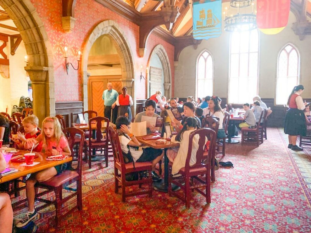 people sitting at dining tables and chairs in elegantly decorated room with banners and red carpet at Cinderellas royal table magic kingdom breakfast