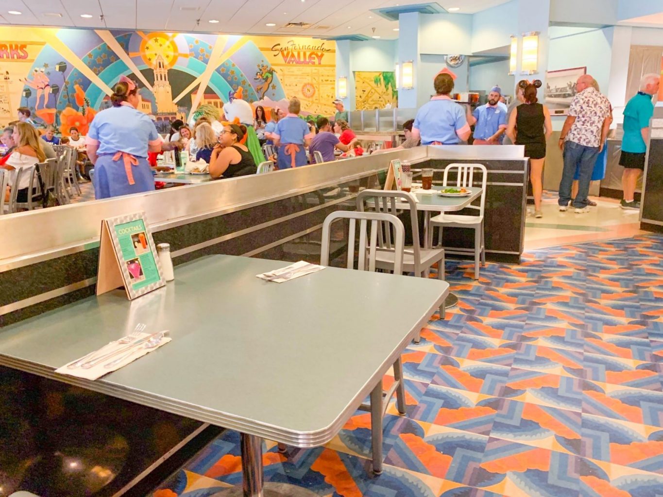 people at metal dining table and standing in line with funky colorful carpet 