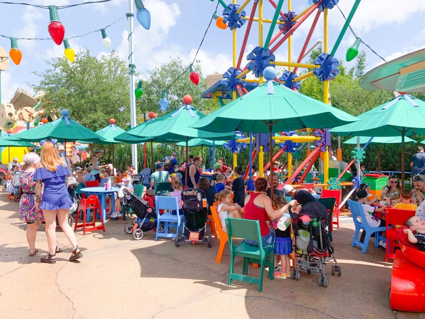 large lightbulbs and toys over green umbrellas with people seated at tables 