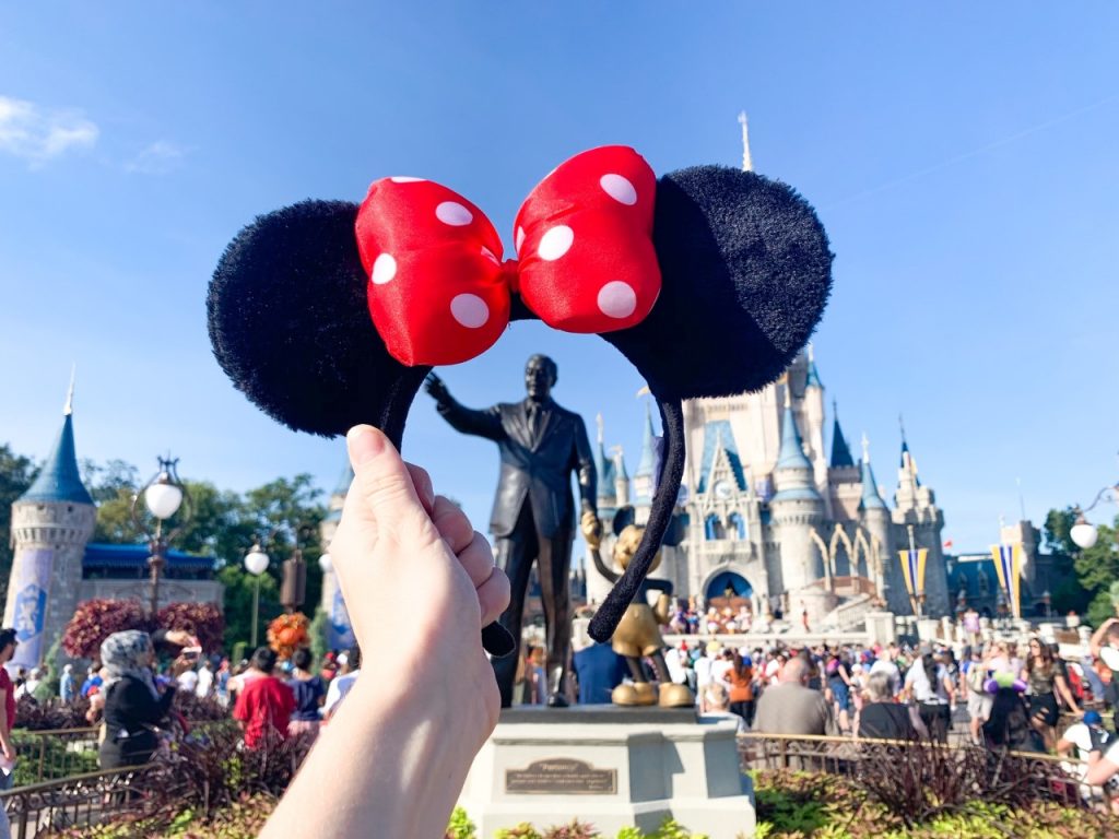 minnie ears held up in front of a statue of Walt Disney and Mickey Mouse