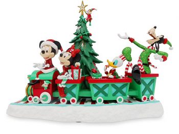Mickey Mouse and his friends ride on a Christmas train figurine in front of a Christmas tree