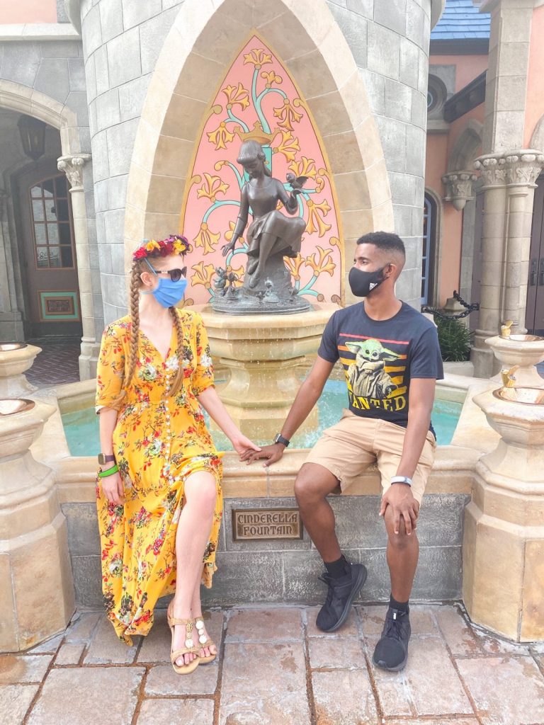 couple sitting in front of the Cinderella statue and fountain near Cinderella's castle