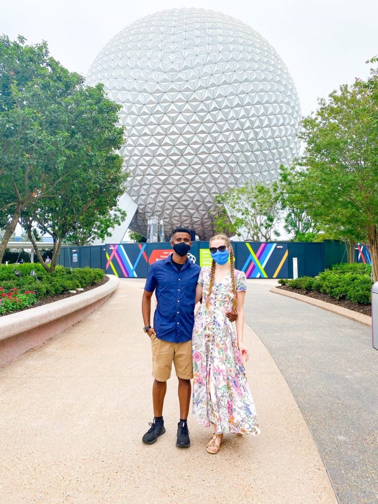 couple standing in front of the Epcot ball and construction walls