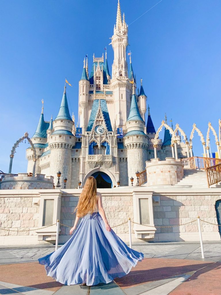 Disney Instagram captions gorgeous photo in front of cinderella's castle, long skirt flowing in the wind