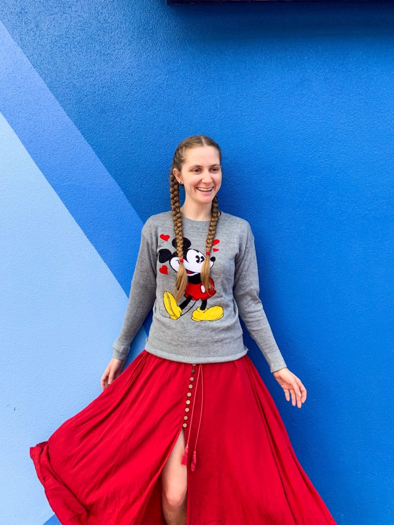 woman standing in a mickey mouse sweater on a blue wall