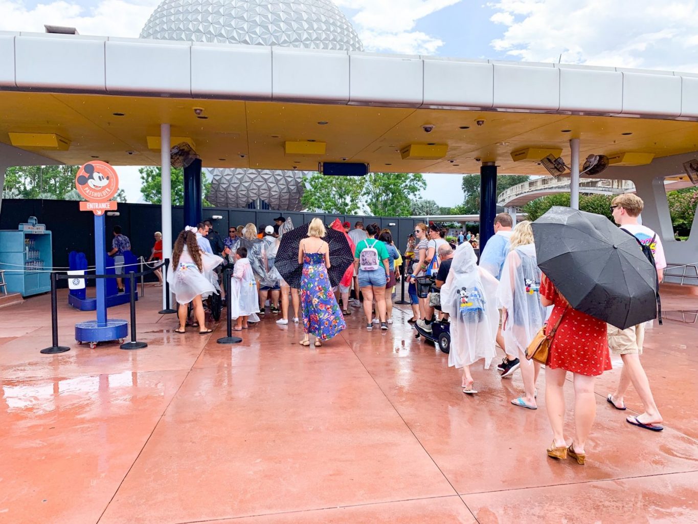 people wearing ponchos and carrying umbrellas while entering Epcot