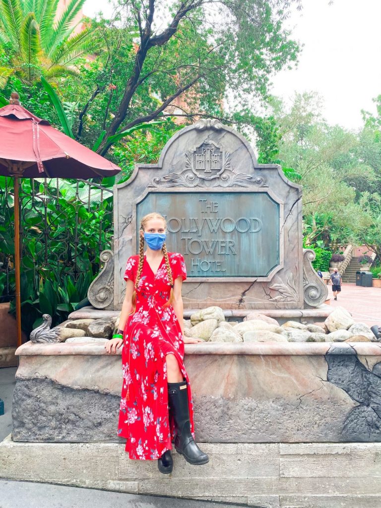 woman wearing rain boots sitting in front of the Hollywood Tower Hotel sign