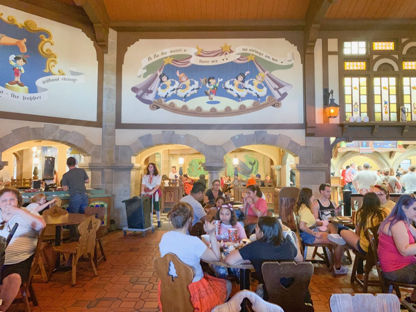 people at tables eating underneath paintings of Pinocchio outdoor dining at disney 
