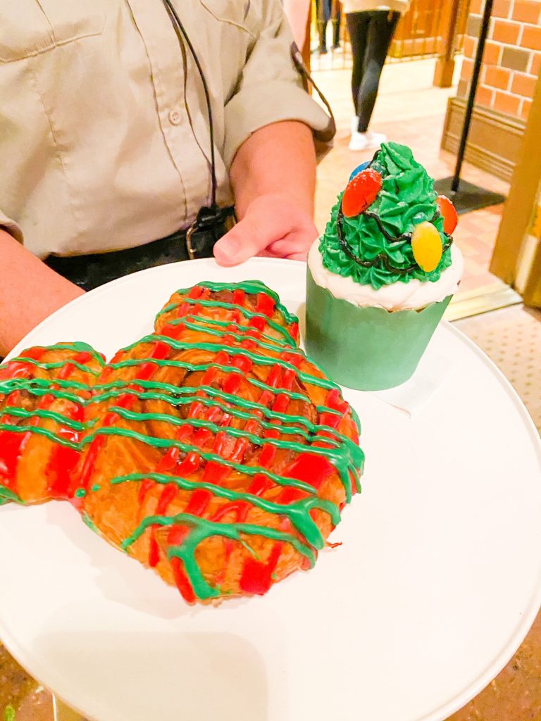 mickey shaped cinnamon roll and christmas tree cupcake on a plate