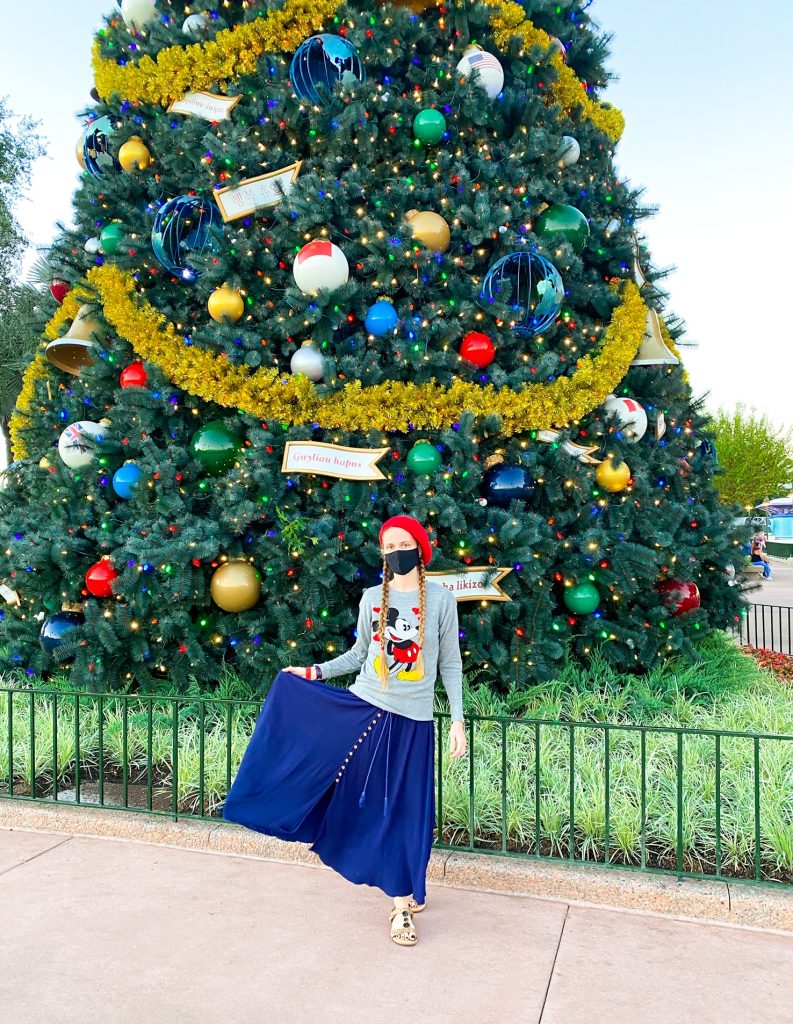 girl wearing sweater and skirt in front of large christmas tree at disney