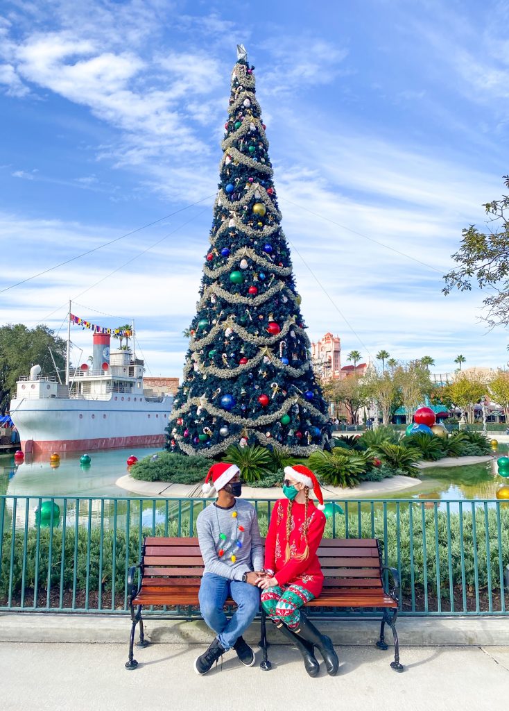 Two people sat on a bench in Hollywood studios with a Christmas tree behind them. 