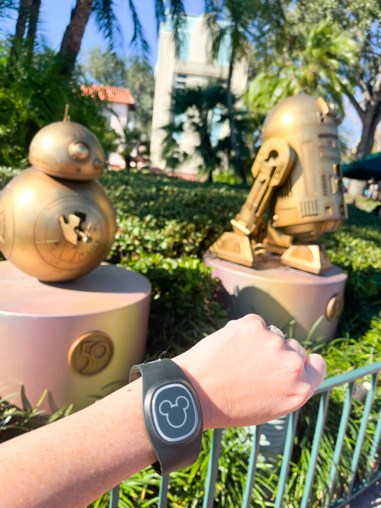 wrist wearing disney magic bands in front of two gold star wars statues