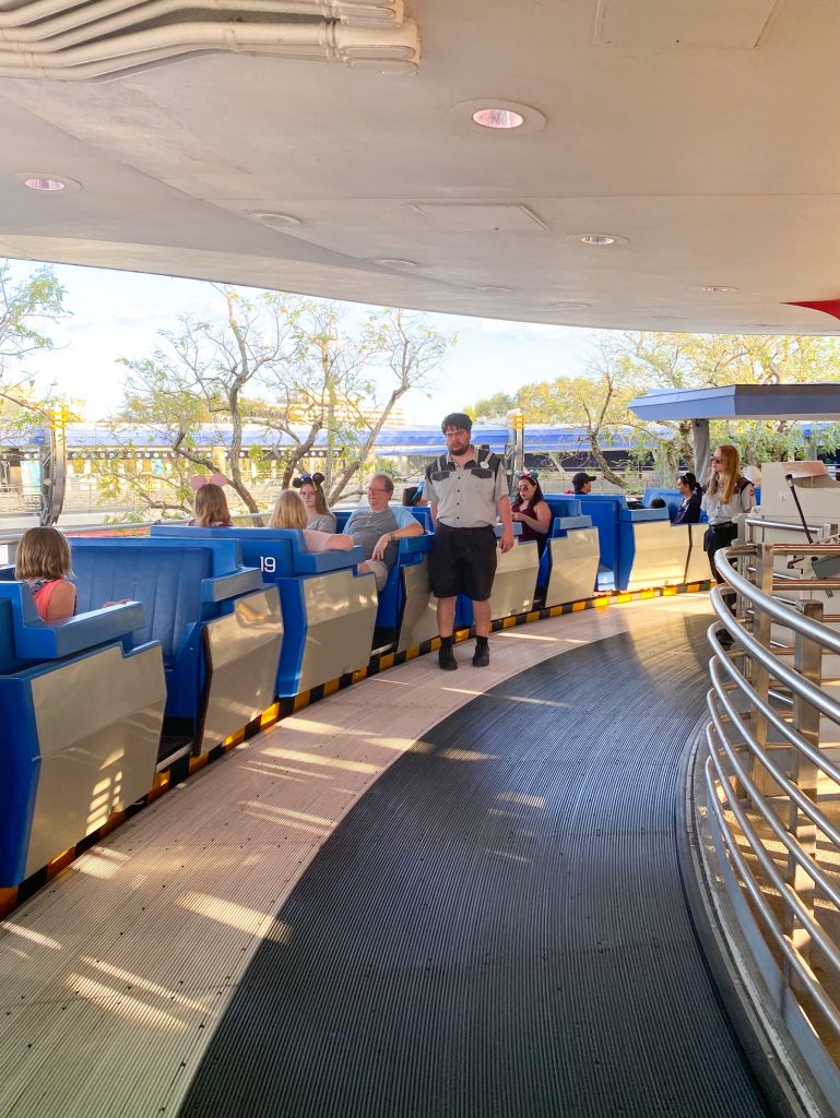cast member loading guests onto moving grey and blue tram
