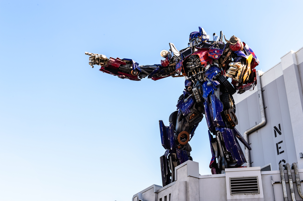 Optomis prime sits on top of the Transformers ride, his robot hand outstretched and pointing. 