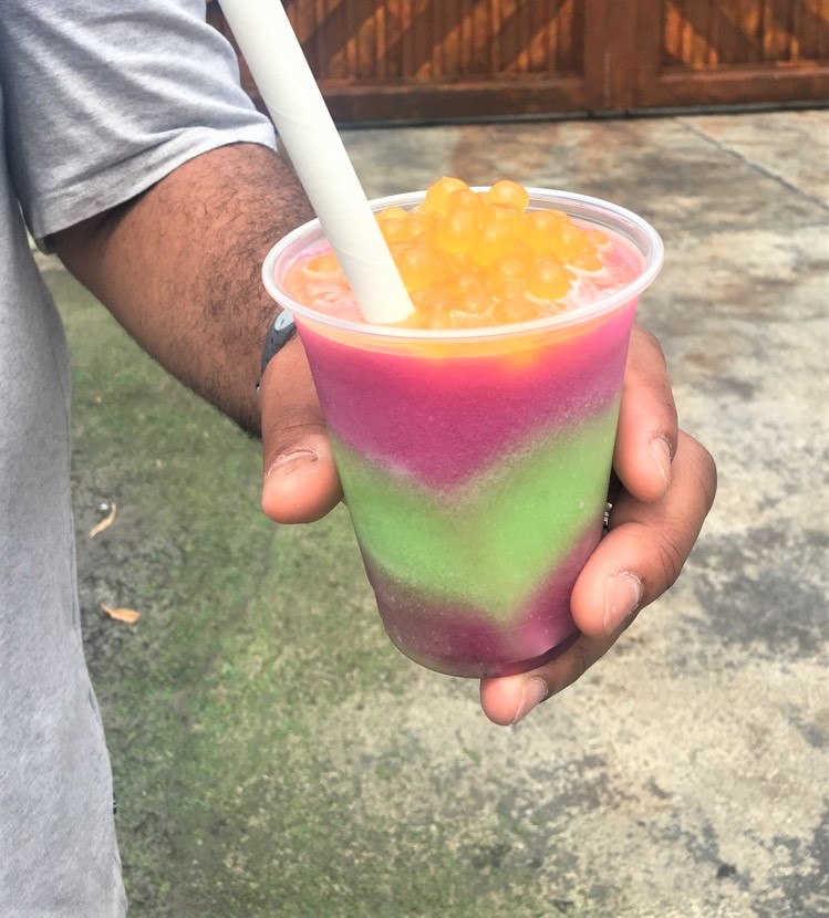 hand holding a purple and green layered drink with orange boba balls on top 