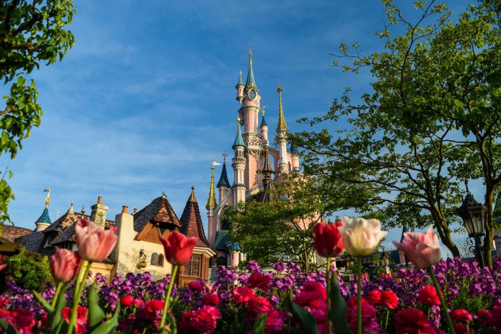 pink and blue castle behind colorful flowers and blue sky Charles de Gaulle to Disneyland Paris